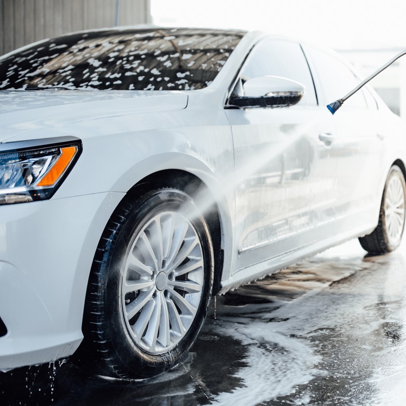 professional-washer-in-blue-uniform-washing-luxury-car-with-water-gun-on-an-open-air-car-wash